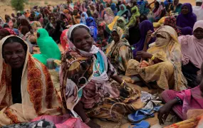 Harana Arabi Souleymane, a Sudanese refugee who is seeking refuge in Chad for a second time, waits to receive food supplements from World Food Programme (WFP) as she chats with other refugees, near the border between Sudan and Chad in Koufroun, Chad, May 11, 2023. She is pictured surrounded by dozens of women, all of which sit on the ground as they wait.